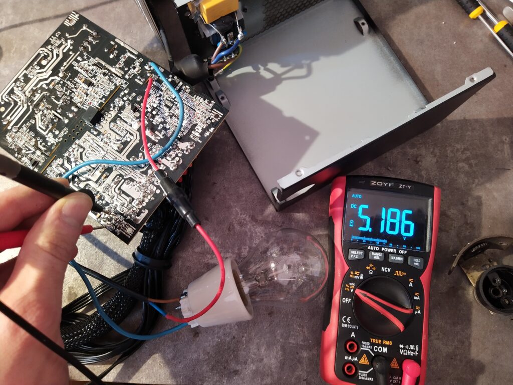 Měření napětí na pomocném zdroji PC zdroje EVGA po opravě. Celý zdroj je připojen k síti přes žárovku 60 W.